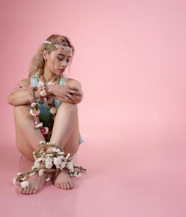 Woman in a serene yoga pose against a soft pink background.